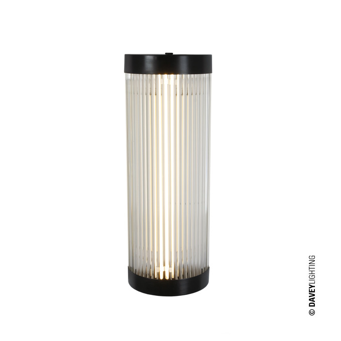 Nástěnná lampička Pillar Wide od Original BTC. Čiré skleněné trubice. Základna a vršek kov. Art Deco styl, vhodná do koupelny. (mosaz s patinou)