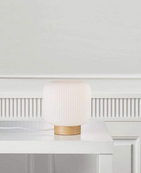 Originální stolní lampičku Milford z bílého opálového skla se skládaným vzhledem ve variantě s dřevěným podstavcem můžete mít v ložnici i vy